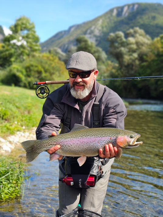 Flugfiskare håller upp en regnbåge vid floden på en fiskeresa till Bosnien med Outside Travels.