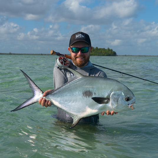 Leende sportfiskare med solglasögon håller stor silverfisk i klart vatten, Ascension Bay Mexiko, perfekt för fiskeresa.