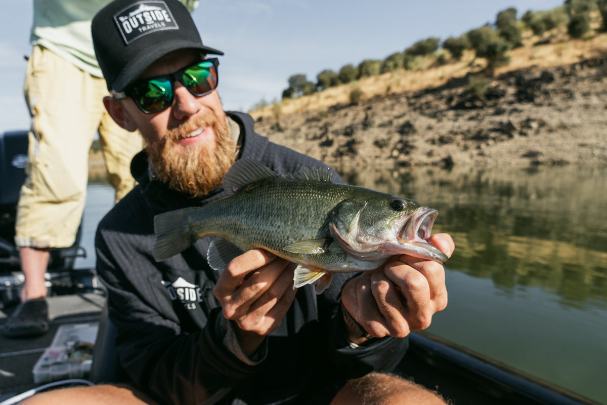 Skäggig sportfiskare med keps håller en largemouth bass i båten i Extremadura