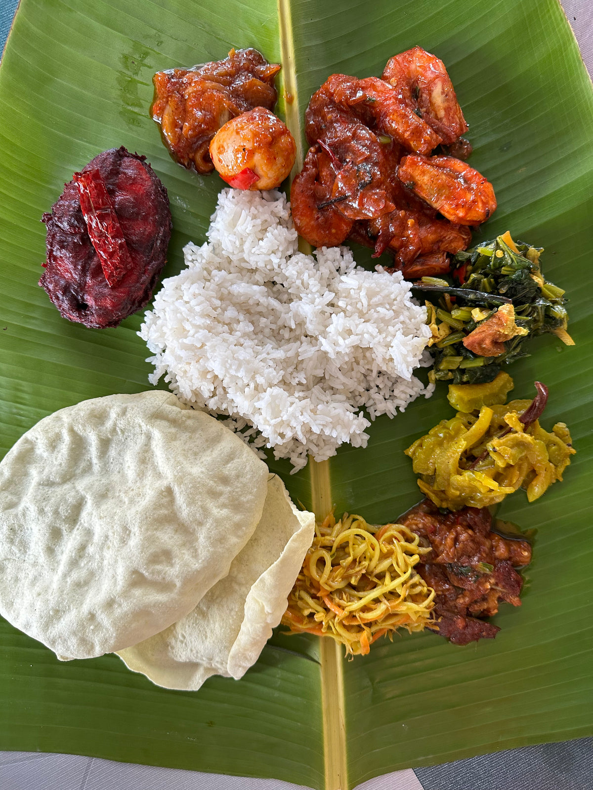 Ris på bananblad med räkor i röd curry, äggcurry, stekt fisk för sportfiskare, grönsaker, bittermelon, nudlar och papadums.