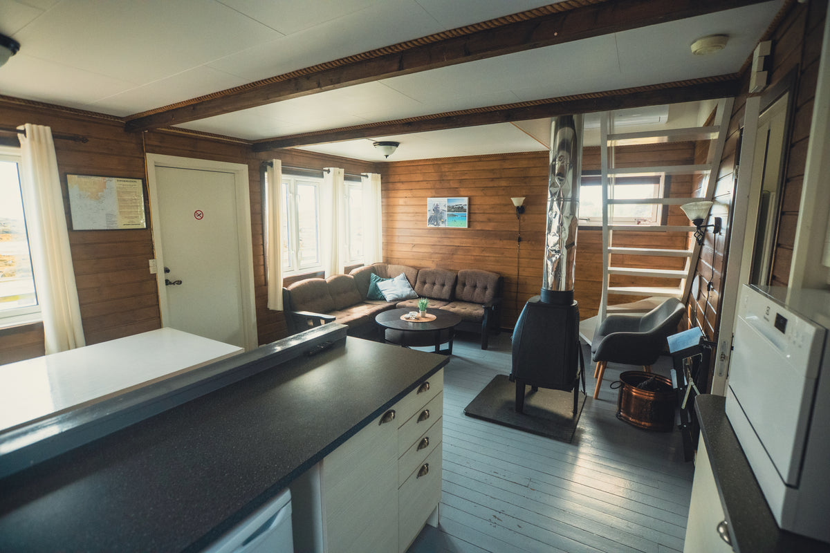 Trivsam trälounge med kamin, soffa, fåtölj, karta och trappa-idealisk för avkoppling efter fiskeresa eller sportfiske.