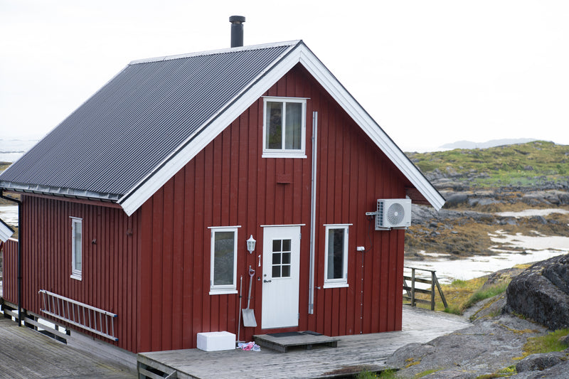 Röd trästuga med mörkt plåttak på altan vid klippig, gräsbevuxen kust-perfekt plats för sportfiskare på fiskeresa.