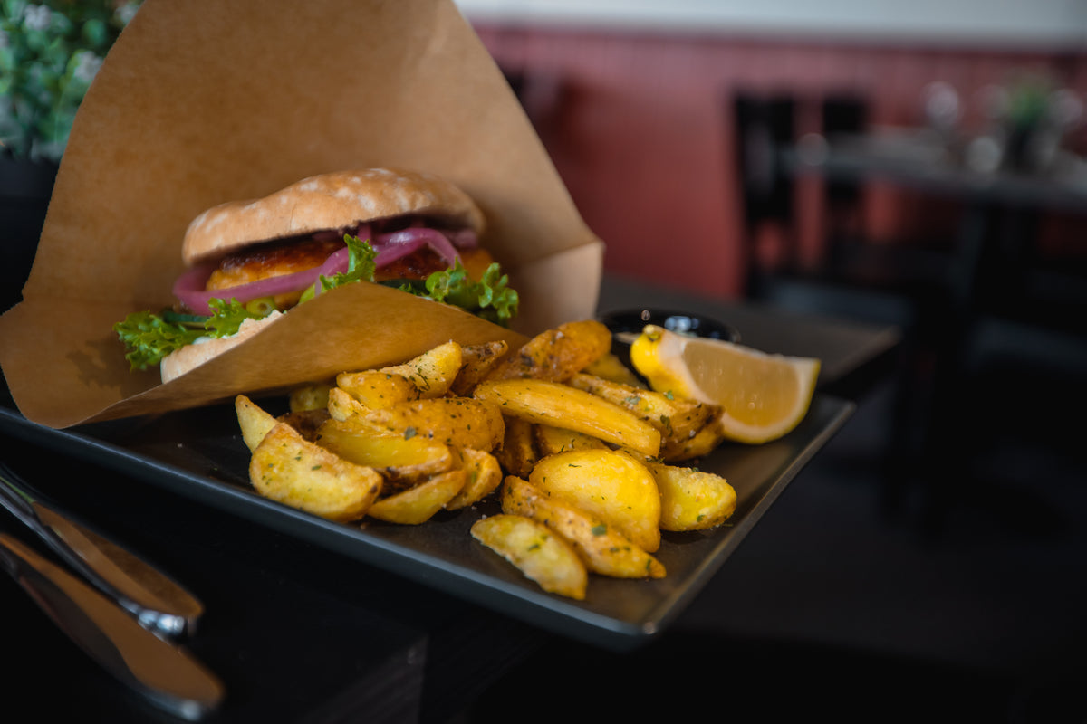 Närbild på smörgås med sallad och rödlök i papper, serverad med kryddade klyftpotatis och citron - energi för sportfiskaren.