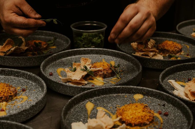 En kock garnerar grå tallrikar med örter, fiskrätter och sås i restaurangkök inspirerat av nordiska fiskeresor.