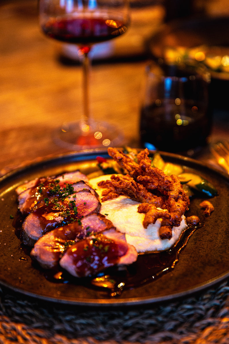 En tallrik med kött i sås, potatismos, stekt lök och grönsaker serveras efter dagens fisketur. Ett glas rödvin och en drink står bredvid på det upplysta bordet – perfekt för att ladda batterierna efter en fisketur.