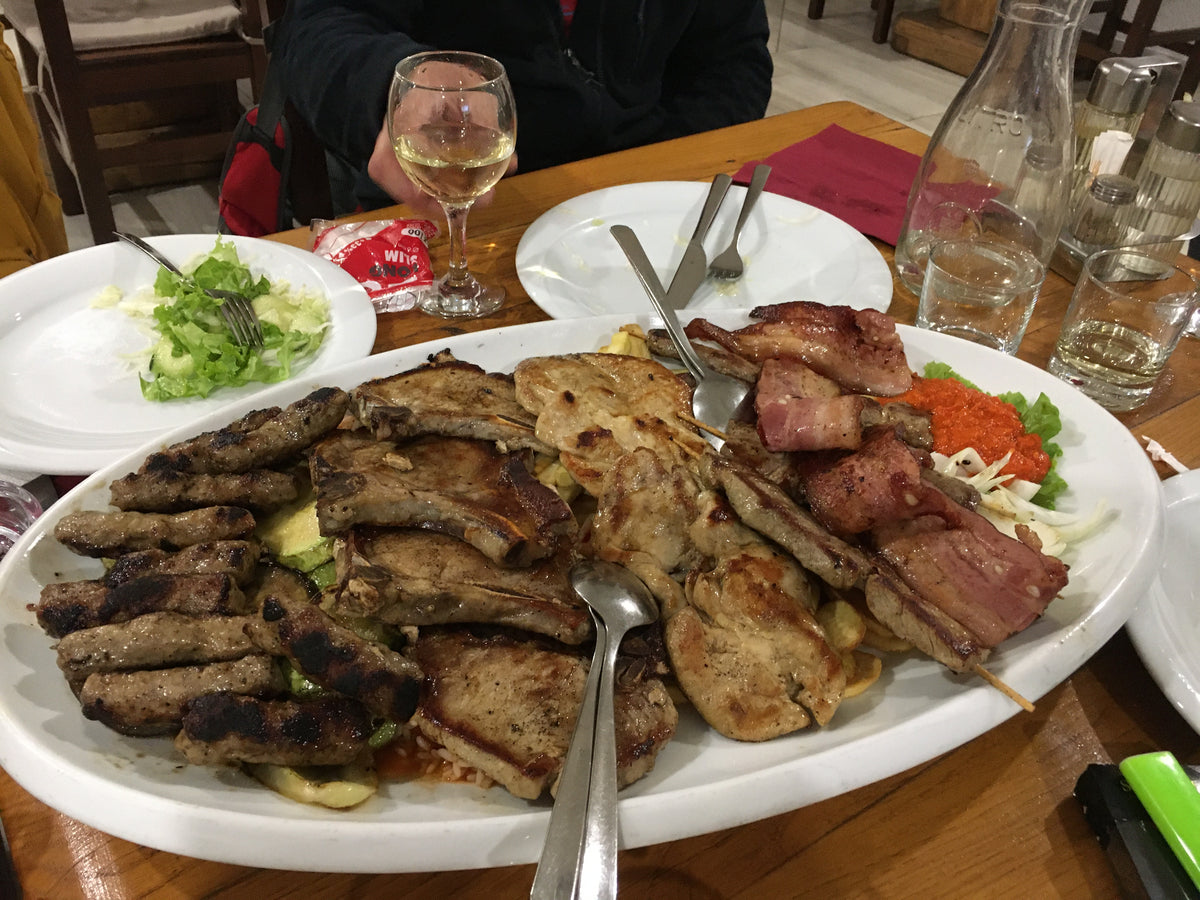 Stort fett med grillat kött på träbord-idealisk middag för sportfiskare efter fiskeresa, med sallad, vin och vatten.