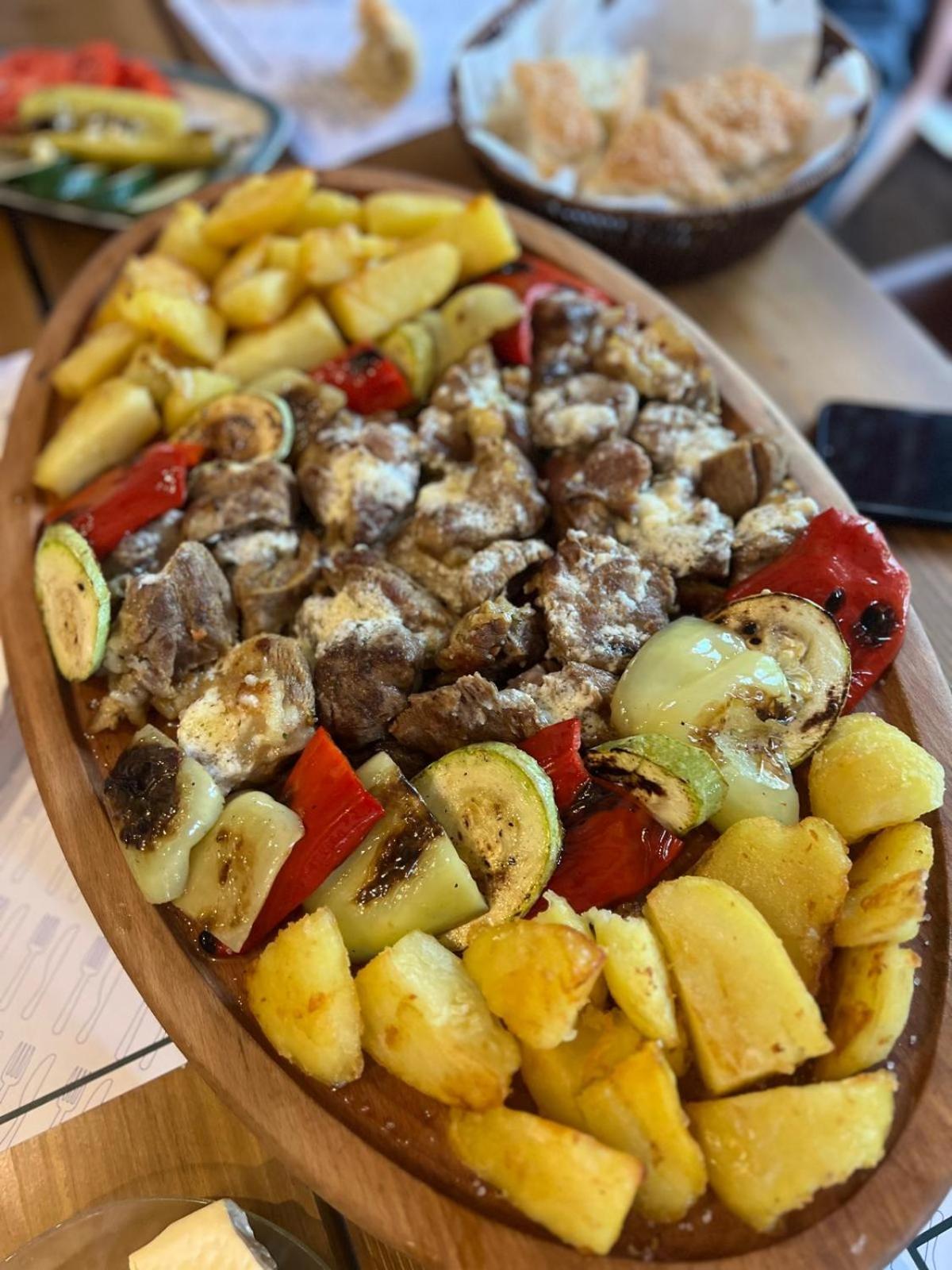 Träfat med grillat kött, rostade potatisar, grönsaker - perfekt måltid efter lyckad fiskeresa. Bröd och mobil i bakgrunden.