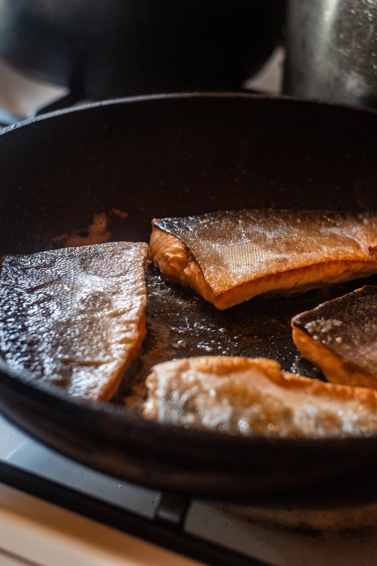Fiskfilébitar steks med skinnsidan nedåt i panna på spis, oljan glittrar - perfekt för sportfiskare efter lyckat fiske.