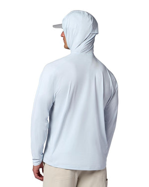 Man i ljusblå Simms Solarflex fiskehoodie med solskydd, beige byxor och keps visar ventilerande tyg mot vit bakgrund.